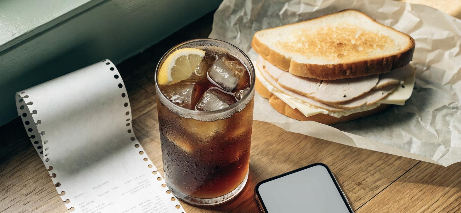 McAlister's Deli guest review survey setup: a paper receipt, a glass of iced sweet tea with lemon and a turkey sandwich on a wooden deli table
